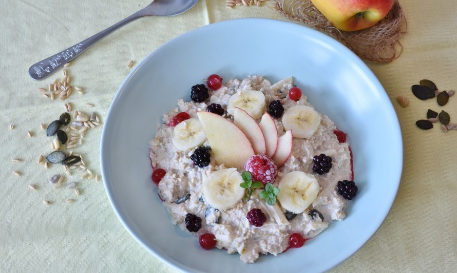 En esta imagen hay un desayuno de avena, frutos rojos y plátano preparado en un plato blanco