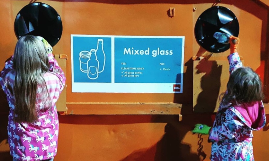 En esta fotografía se ve a Eloise junto a una amiga reciclando vidrios en un contenedor. Ellas son tan pequeñas, que deben alcanzar el alto contenedor con ayuda de unos banquillos