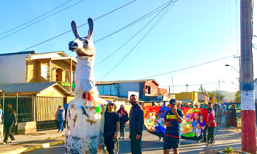 En esta fotografía se puede apreciar una performance artística en el pasacalles del Carnaval Autogestionado de Coquimbo: un guanaco gigante hecho de materiales reciclados es controlado por tres artistas locales